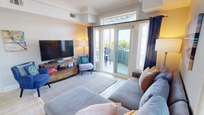 Sala de estar con televisor de pantalla plana, sofá, sillón y mesa de centro. Hay una puerta corrediza de vidrio que da a un área exterior.