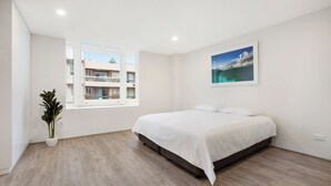 Una camera da letto moderna con un letto grande, una pianta in vaso, una finestra vista edifici e un quadro appeso al muro.