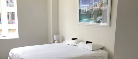 Habitación de hotel minimalista con una cama grande, una mesita de noche, una lámpara de pared y un cuadro enmarcado.
