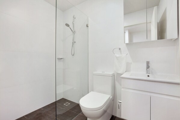 Une salle de bain moderne avec une douche en verre, des toilettes blanches et un lavabo surmonté d’un miroir.