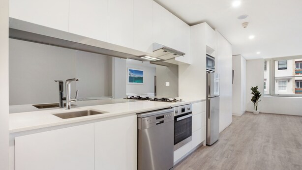 Una cucina moderna con mobili bianchi, elettrodomestici in acciaio inossidabile e un'ampia finestra che offre luce naturale.