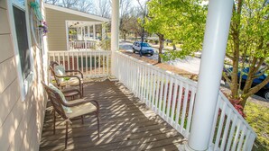 Eine hölzerne Veranda mit weißer Holzbalustrade, zwei Korbstühle und eine kleine überdachte Sitzecke mit einer Bank.