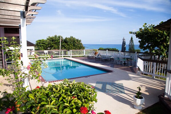 A pool area with a view of the ocean, surrounded by a white fence and potted plants.