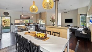 Una cocina moderna con una isla central, comedor con una mesa blanca y sala de estar con sofá y televisor.