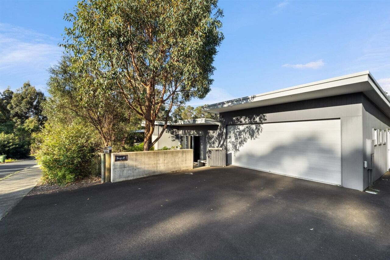 A modern building with a large garage door, surrounded by a paved driveway and a tree.