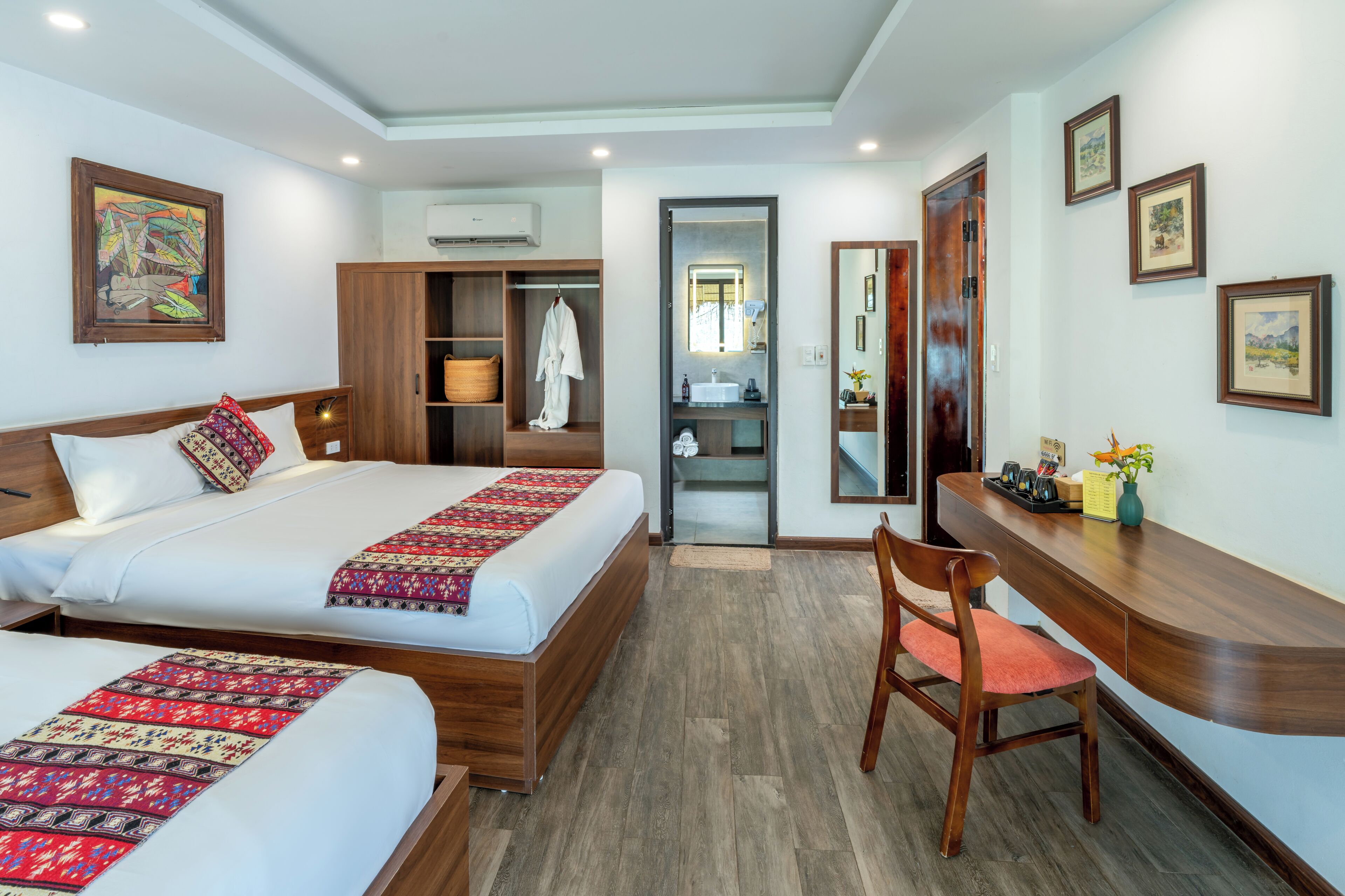 A hotel room with two beds, a desk, a chair, a wardrobe, and a bathroom.