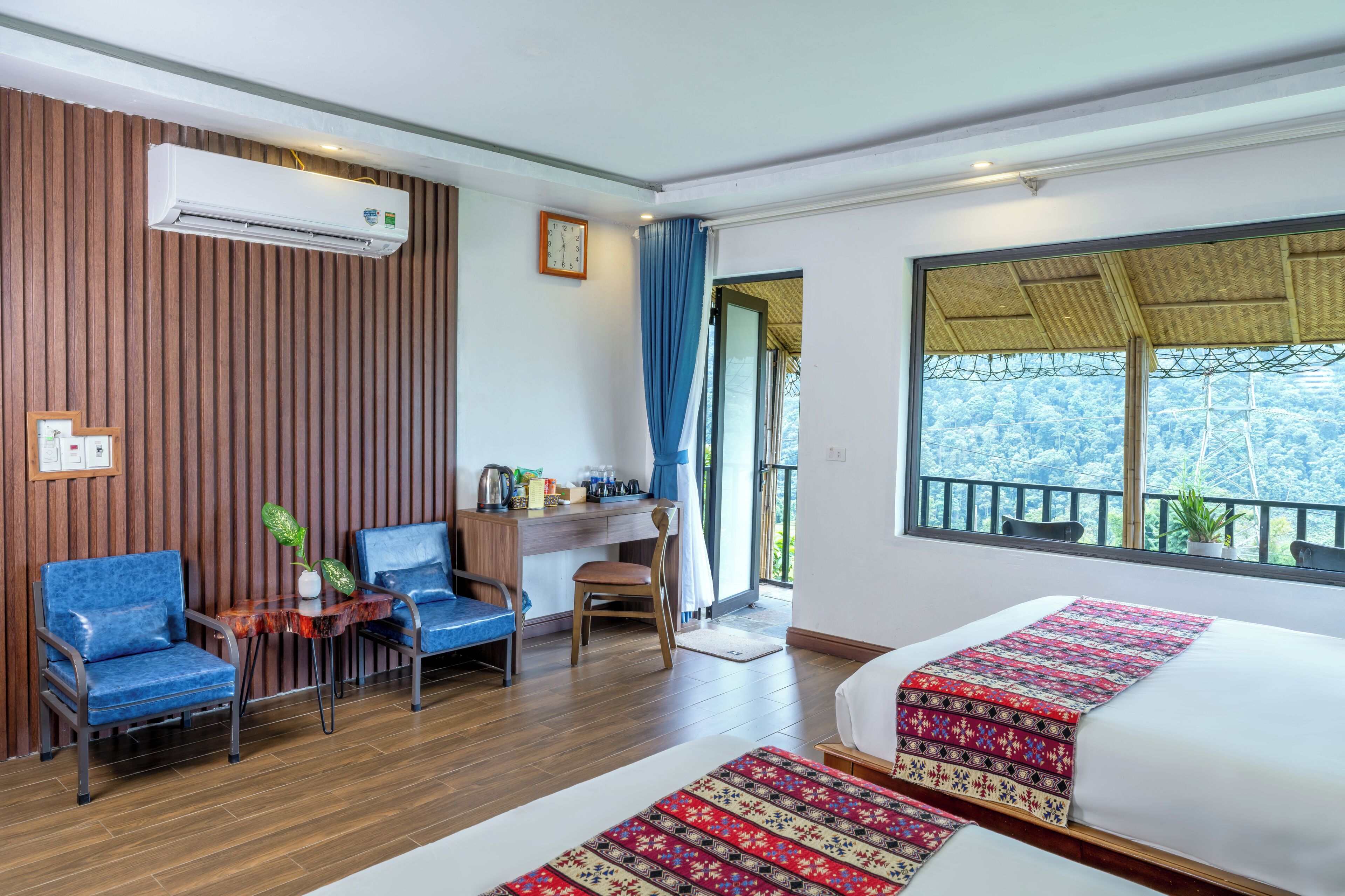 Ein Hotelzimmer mit zwei Betten, einem Schreibtisch, einem Stuhl, einer Uhr und Blick ins Freie.