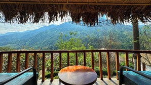 A wooden deck with a thatched roof, a round table, and two benches, overlooking a mountainous landscape. -  Belle Maison Sapa Resort & Spa - Formerly Sapa Eco Villas & Spa (Ta Van)