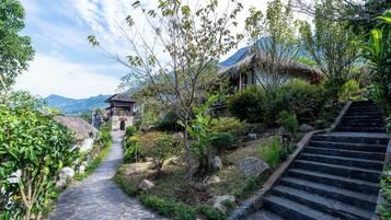 A stone pathway leading to a traditional thatched-roof building with a sign reading 'HÀM RƯU'.