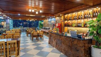 Un restaurante con piso a cuadros, mesas y sillas de madera, una zona de bar con botellas y un ordenador portátil sobre la barra.