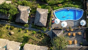 Vista aérea de un complejo turístico con piscina, estructuras de techo de paja y zonas de estar al aire libre.