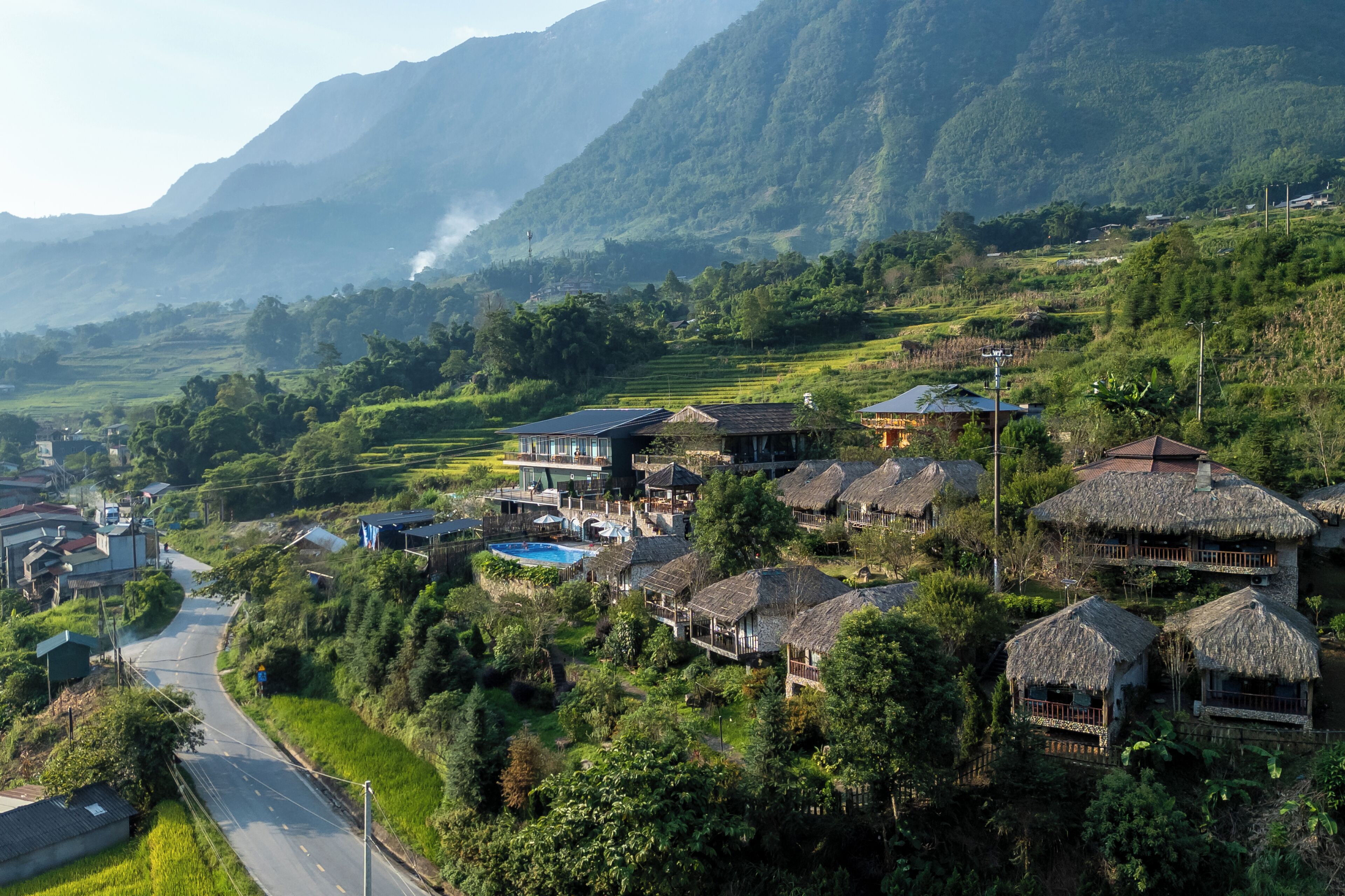 A rural village with traditional thatched-roof houses, a swimming pool, and terraced fields.