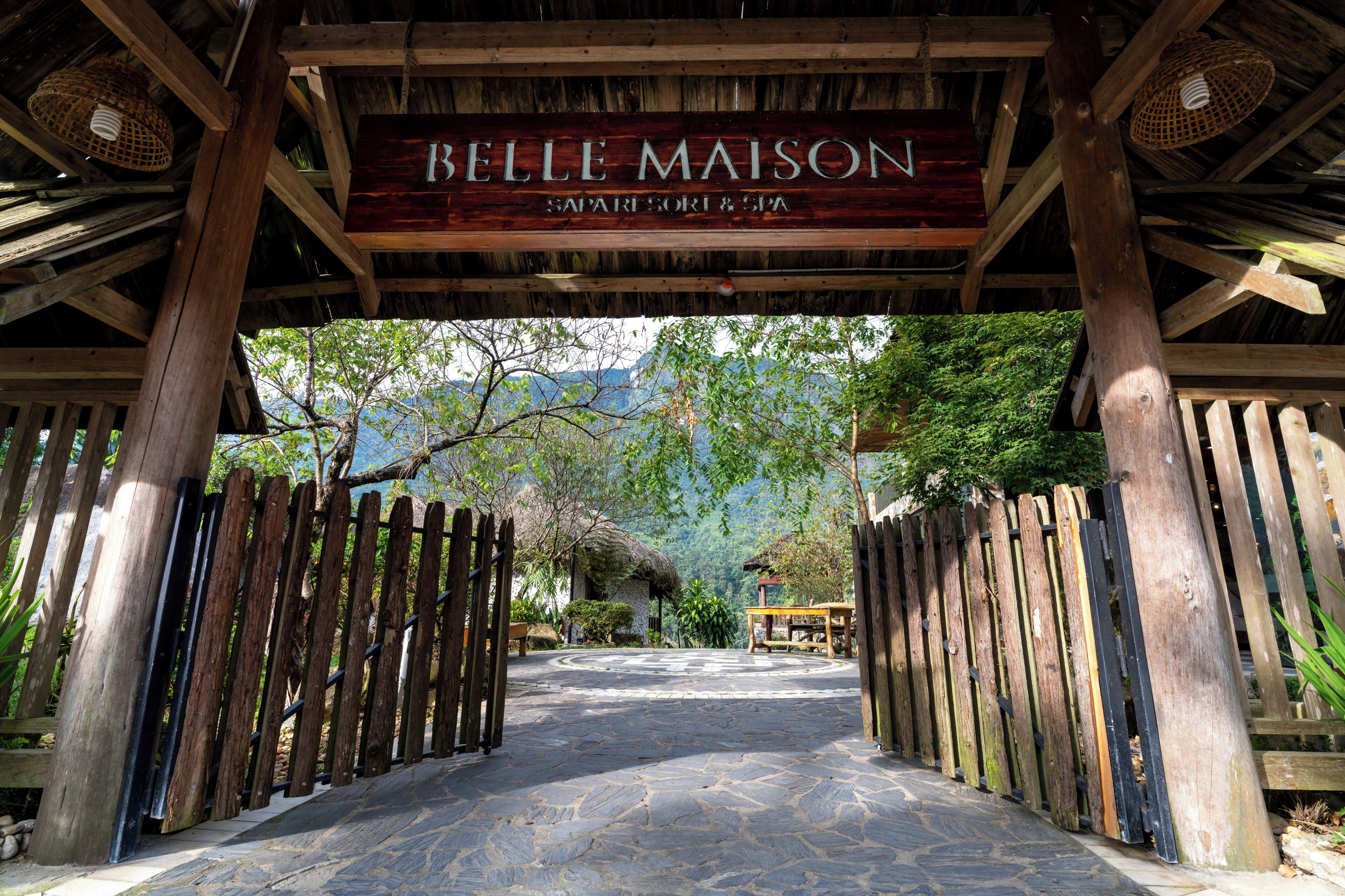 A wooden archway with a sign reading 'BELLE MAISON SPA & SORRY' leading to a stone-paved path.