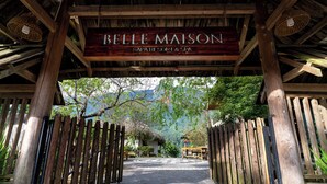 Un arco de madera con un letrero que dice 'BELLE MAISON SPA & SORRY' que da paso a un camino empedrado.