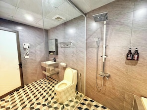 Un baño moderno con inodoro, lavabo, espejo, ducha y suelo de baldosas.