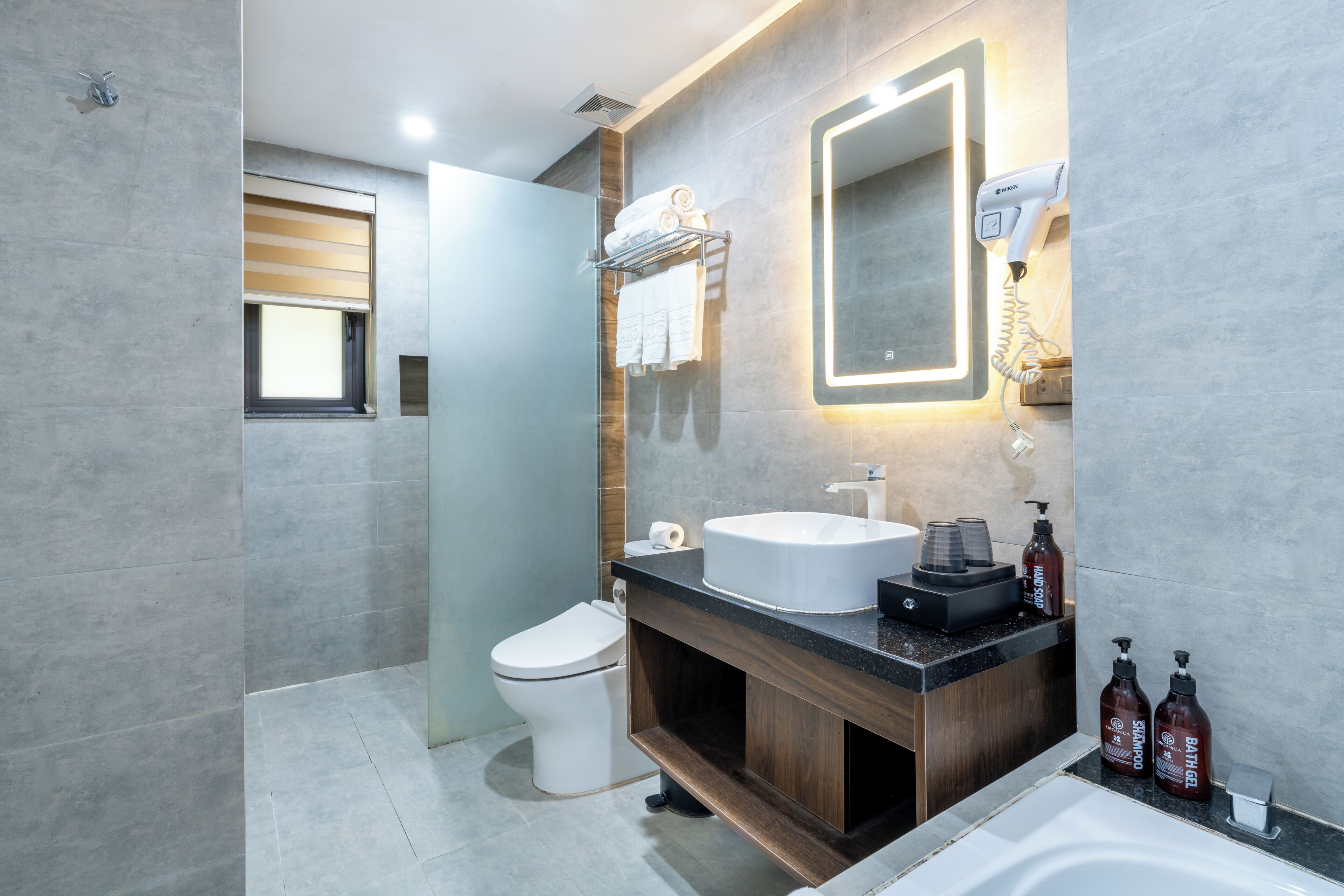 A modern bathroom with a toilet, sink, and bathtub. There is a mirror above the sink and a towel rack with towels.