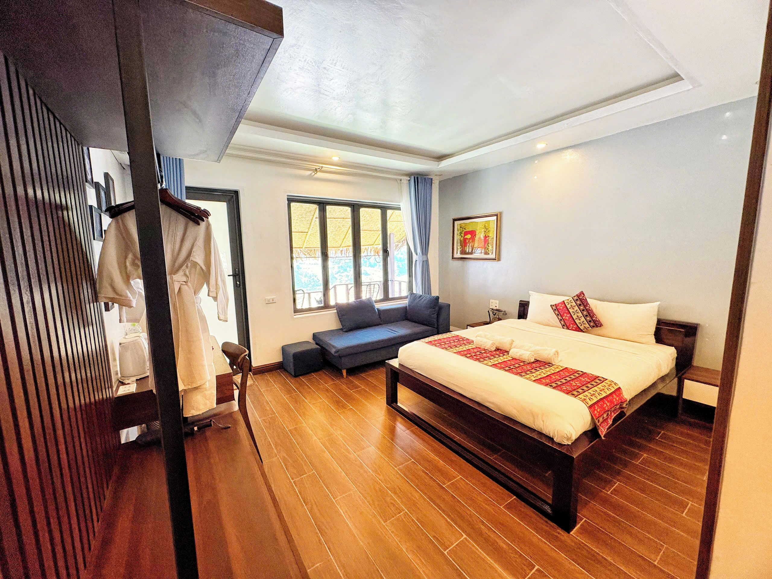 A bedroom with a large bed, a sofa, a wooden floor, and a window with curtains.