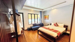 Un dormitorio con una cama grande, un sofá, suelo de madera y una ventana con cortinas.
