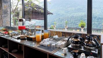 A breakfast bar with various food items, a coffee machine, and a view of a mountainous landscape.
