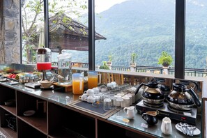 A breakfast bar with various food items, a coffee machine, and a view of a mountainous landscape.