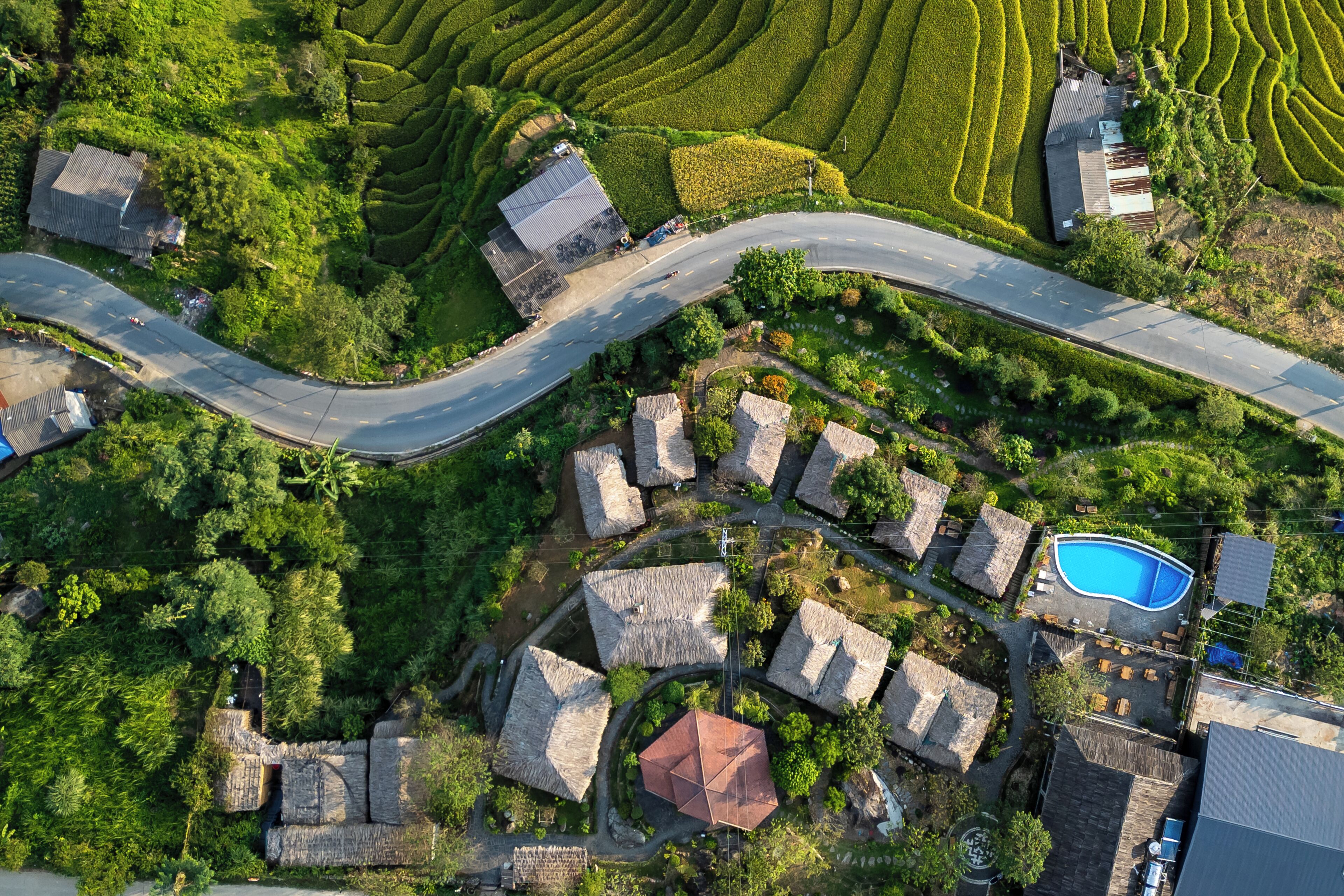 A residential area with a winding road, houses with thatched roofs, and a swimming pool.