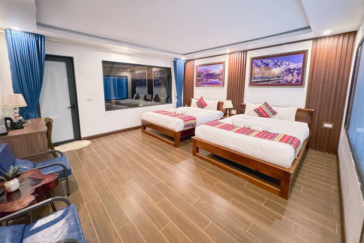 A hotel room with two beds, a desk, a chair, and a window with a view of a mountain landscape.