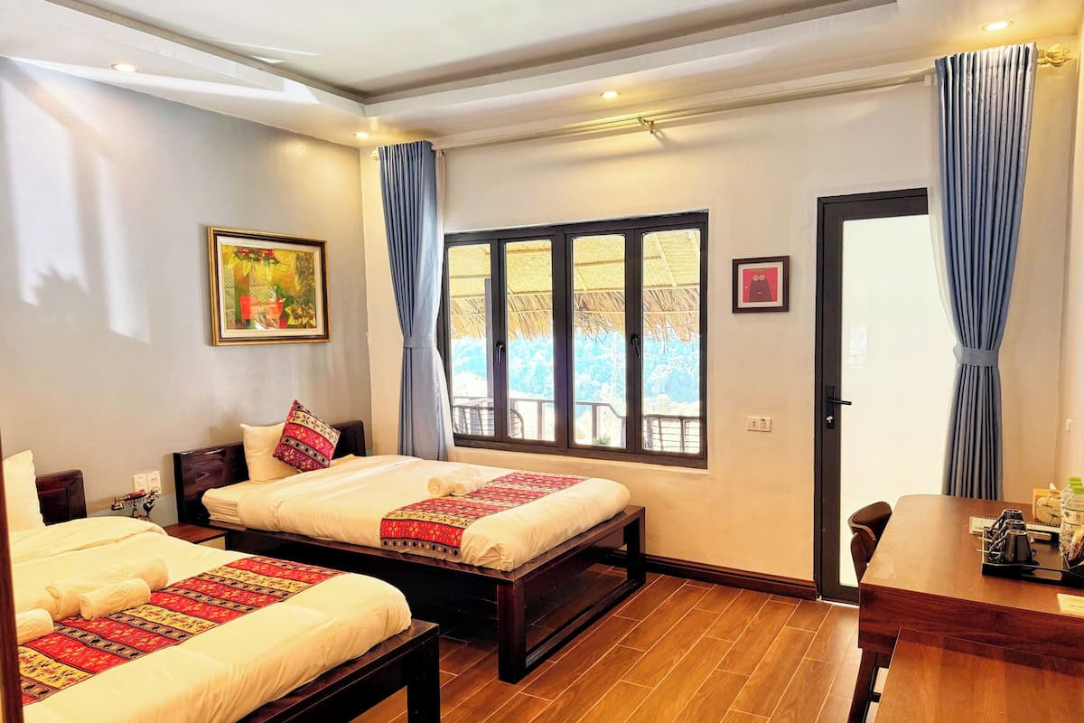 A hotel room with two beds, a wooden floor, a dining table, and a large window with curtains.