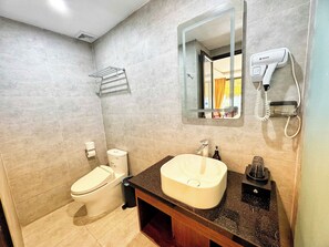 Un baño con inodoro, lavamanos, espejo, toallero y secador de pelo.