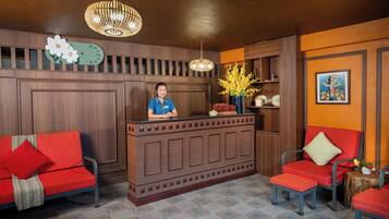 A reception area with a wooden reception desk, two red upholstered chairs, a clock, and a vase with yellow flowers.