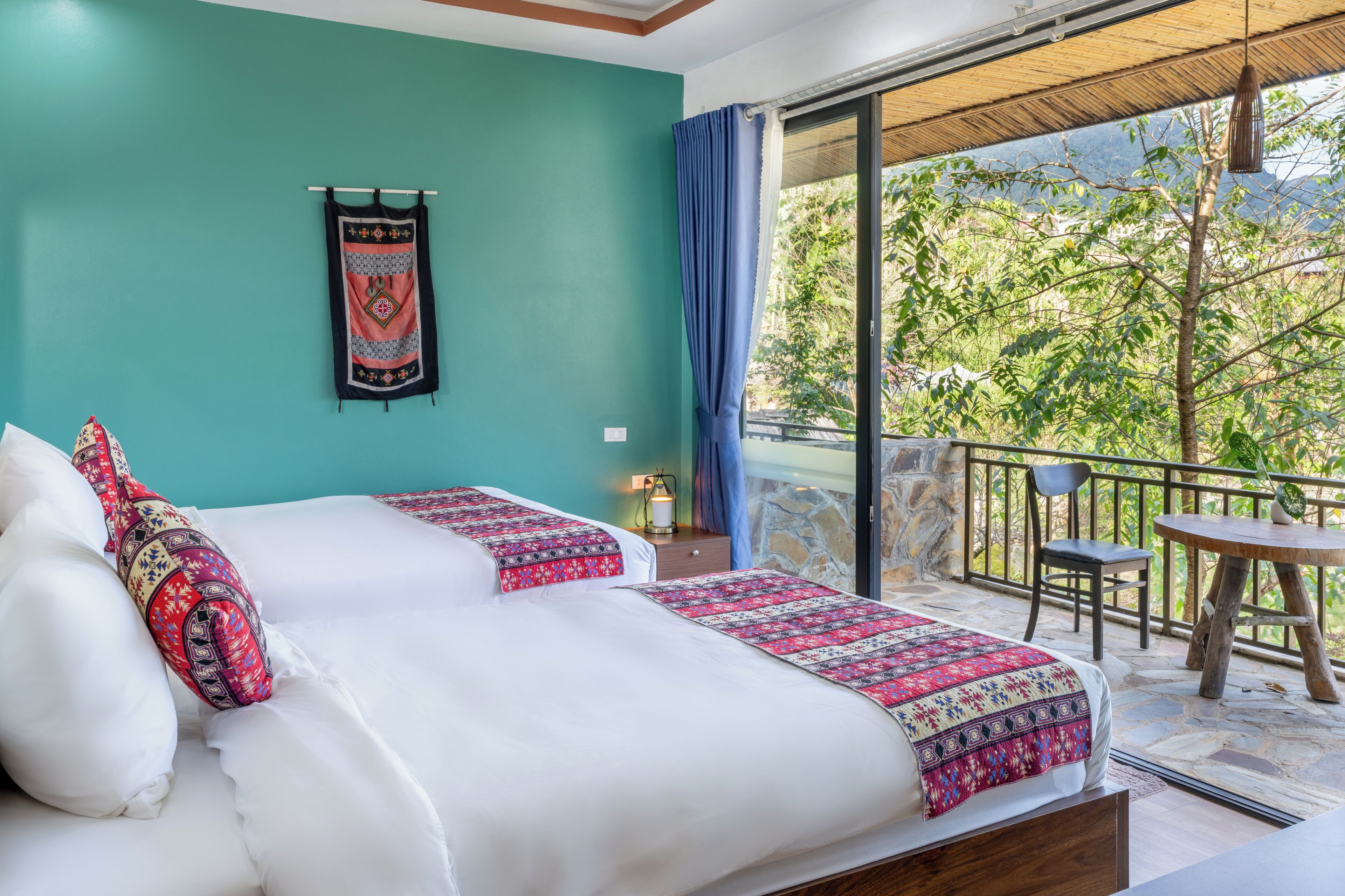 A bedroom with a bed, a nightstand, a window with curtains, and a balcony with a table and chair.