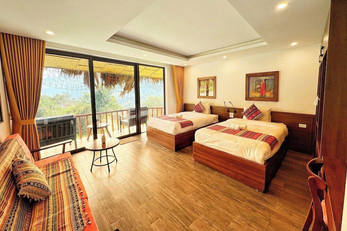 Habitación de hotel con dos camas, un sofá, una mesita y un balcón con vistas.