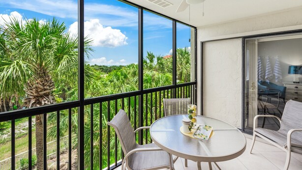 Un balcon avec une table et des chaises, un ventilateur de plafond et une vue sur la verdure.