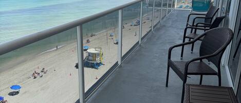 A balcony with wicker chairs overlooking a beach with umbrellas and a lifeguard stand.
