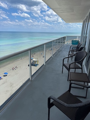 A balcony with wicker chairs overlooking a beach with umbrellas and a lifeguard stand.