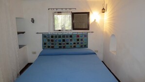 Une chambre à coucher avec un lit, une fenêtre, une lampe fixée au mur et une tête de lit matelassée.