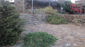 Un bâtiment en pierre doté d’un patio couvert, d’un escalier menant à l’entrée et entouré de verdure.