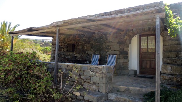 Une maison en pierre avec un porche couvert, deux chaises à rayures et une porte en bois.