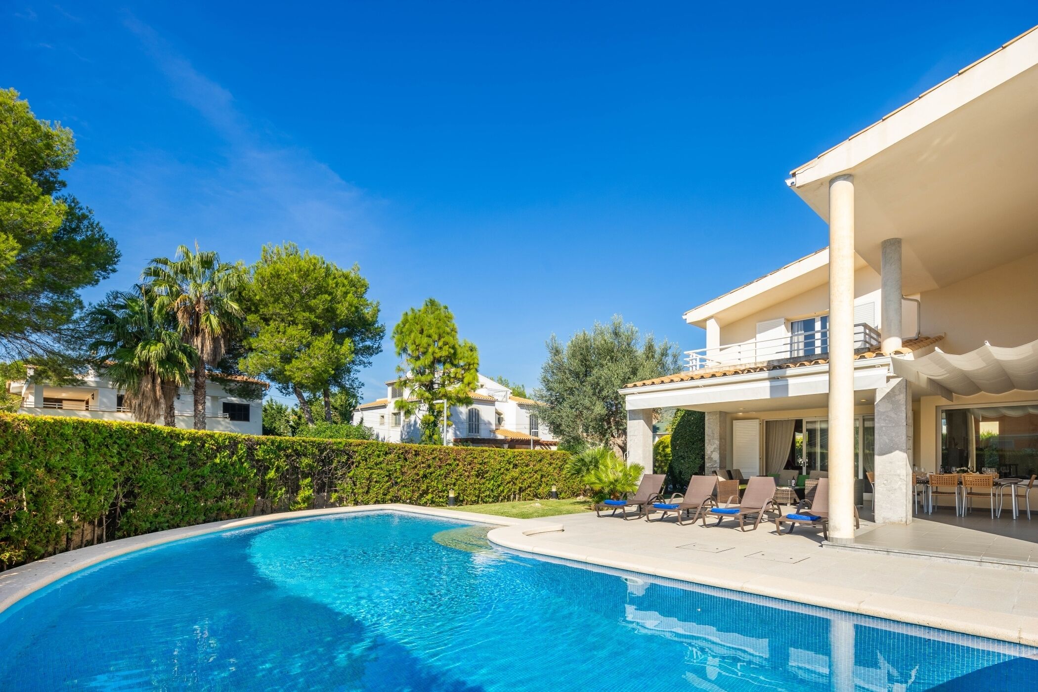 A swimming pool with lounge chairs, a covered patio, and a view of residential buildings.