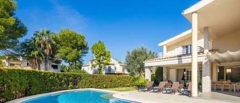 A swimming pool with lounge chairs, a covered patio, and a view of residential buildings.