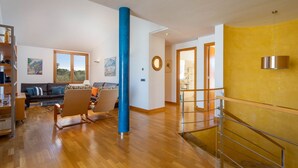 A spacious living area with a wooden floor, a blue pillar, a sofa set, and a staircase leading to another level. - Villa Can Monxo By SunVillas Mallorca (Port de Pollença)