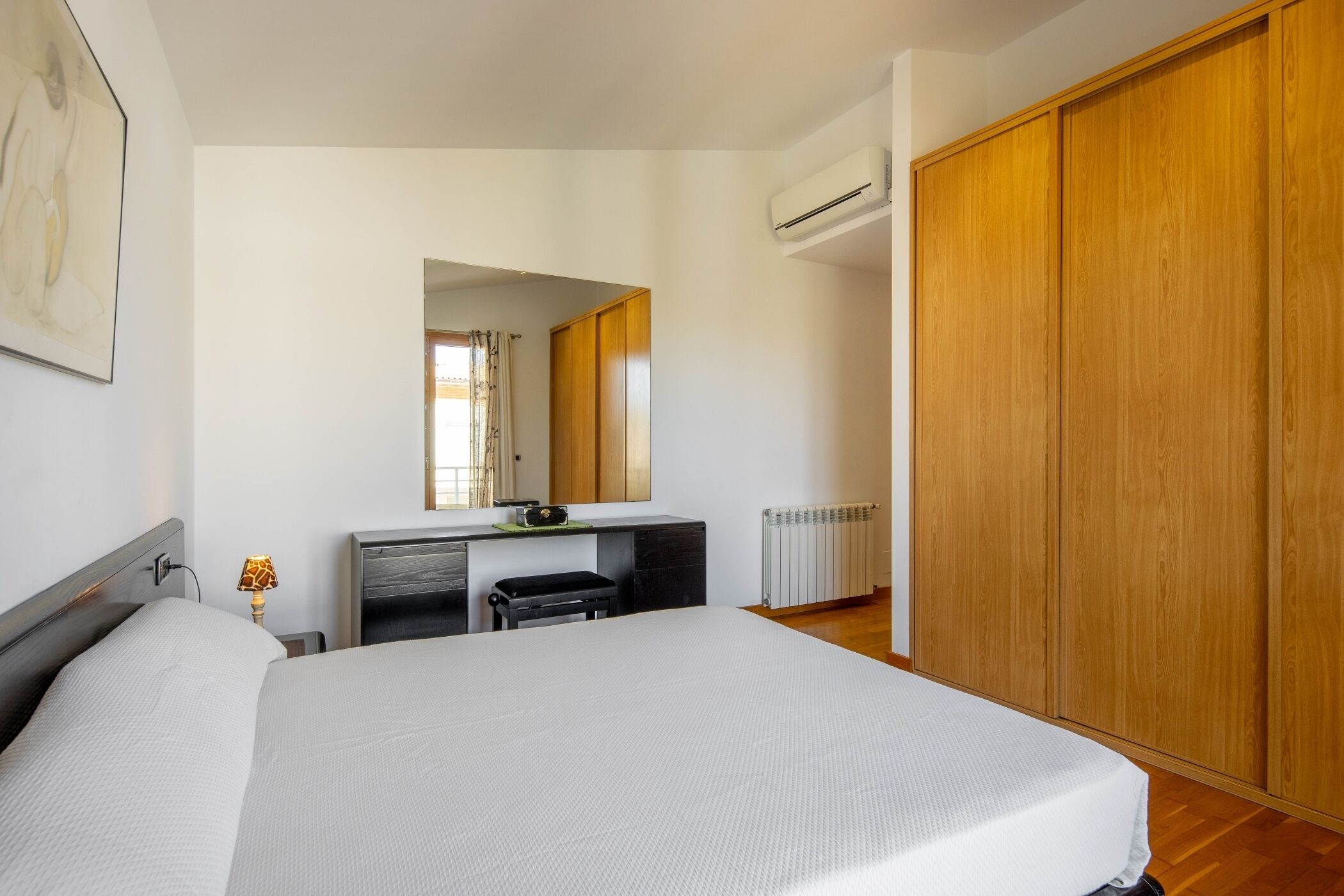 A bedroom with a bed, a desk, a mirror, and a wardrobe.