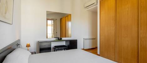 A bedroom with a bed, a desk, a mirror, and a wardrobe.