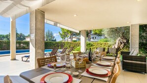 An outdoor dining area with a pool view, tables set with red and white plates, and wicker furniture. - Villa Can Monxo By SunVillas Mallorca (Port de Pollença)