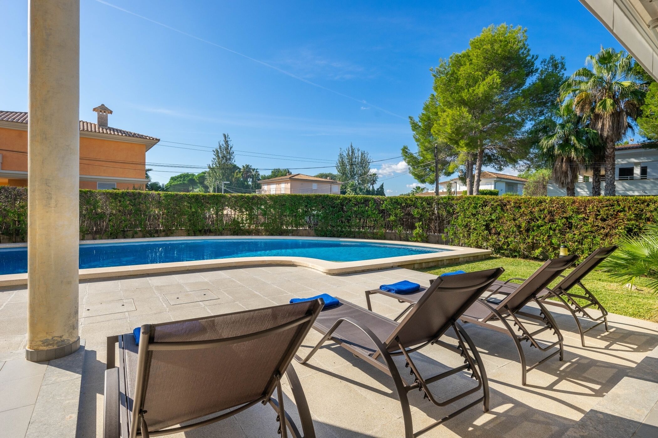 A swimming pool with lounge chairs, a tiled deck, and a hedge.