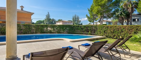 A swimming pool with lounge chairs, a tiled deck, and a hedge.
