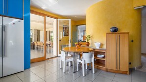 A modern kitchen with a round dining table, white chairs, and a blue cabinet. - Villa Can Monxo By SunVillas Mallorca (Port de Pollença)