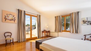 A bedroom with a large bed, wooden floor, a desk with a chair, and a view through the glass door. - Villa Can Monxo By SunVillas Mallorca (Port de Pollença)