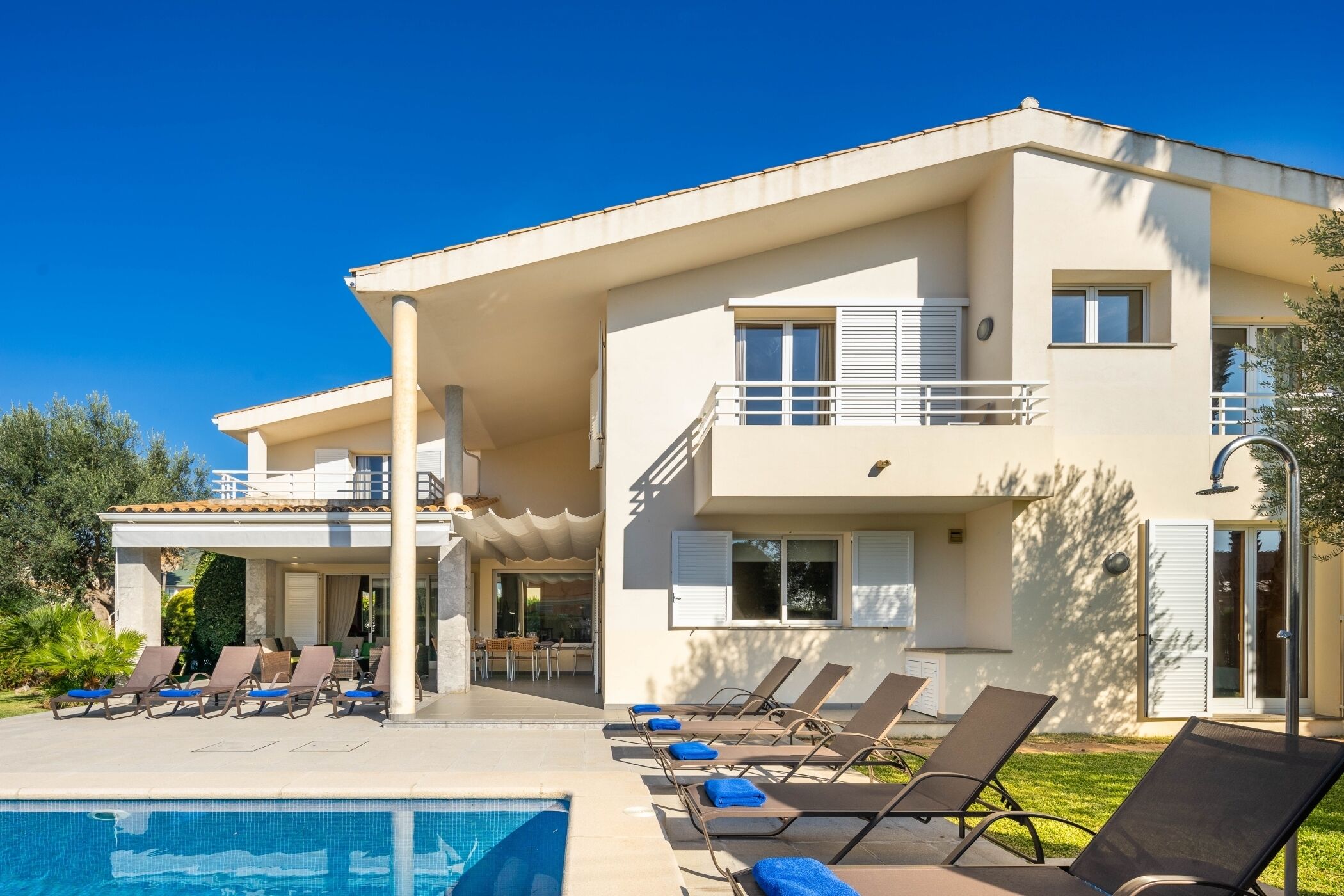 A modern two-story house with a swimming pool, sun loungers, and a covered patio area.