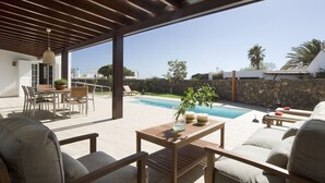 A covered outdoor patio with a pool, wooden furniture, and a stone wall. - Magnificent and spacious Pearl Villa with heated pool, Wifi and AC (puerto del carmen)