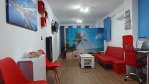 A room with a red sofa, a red chair, a small white table, a TV on the wall, and a painting of a bridge. - Beautiful studio in Triana (Sevilla)